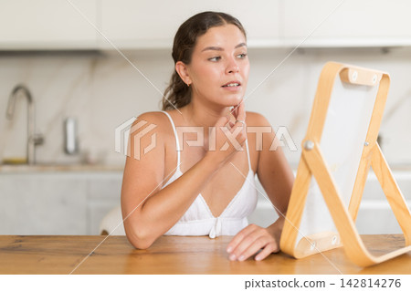 Young woman looking at mirror in kitchen Young woman looking at mirror in kitchen 142814276