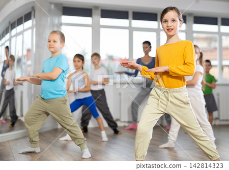 Positive juvenile girl engaged in hip-hop dance in training room with children's group Positive juvenile girl engaged in hip-hop dance in training room with children's group 142814323