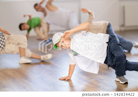 Sporty ten years old boy training breakdance movements of vigorous dance on floor during group class with male teacher in dance school Sporty ten years old boy training breakdance movements of vigorous dance on floor during group class with male teacher in dance school 142814422