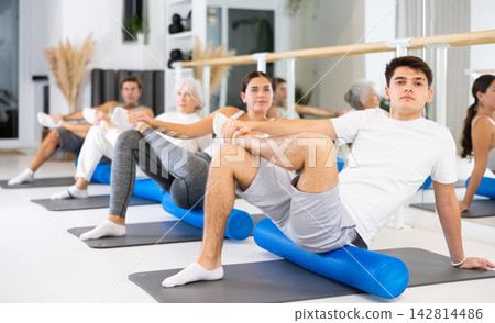 Active vigorous man performs exercises with a pilates roller while on a mat in the hall of a modern fitness studio. Active vigorous man performs exercises with a pilates roller while on a mat in the hall of a modern fitness studio. 142814486