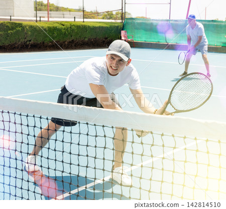 Man in shorts and t-shirt playing tennis on court. Racket sport training outdoors Man in shorts and t-shirt playing tennis on court. Racket sport training outdoors 142814510