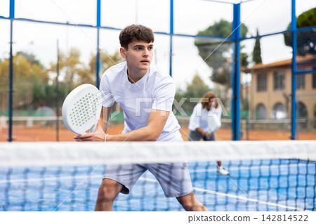 Male player ready to hits the ball while playing padel on hard court Male player ready to hits the ball while playing padel on hard court 142814522
