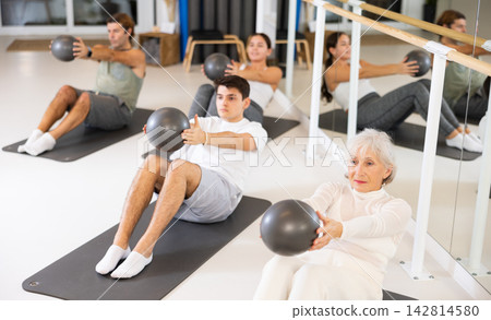 Men and women doing pilates exercises with fitness ball at gym 142814580