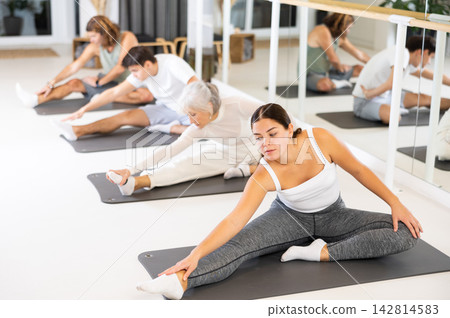 Positive young female performing set of exercises on a pilates mat during group class in fitness studio. Positive young female performing set of exercises on a pilates mat during group class in fitness studio. 142814583