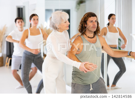 Female ballet teacher showing moves in front of group of different aged dancers in dancing studio Female ballet teacher showing moves in front of group of different aged dancers in dancing studio 142814586