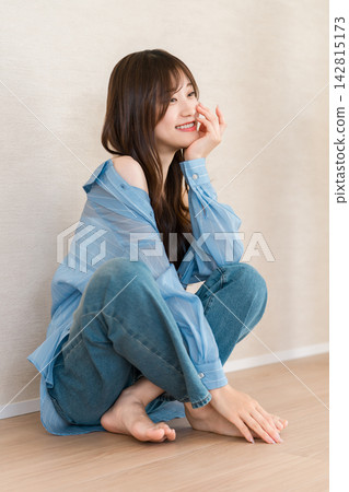 一位女士微笑著坐著，穿著藍色襯衫和牛仔褲，休閒時尚，令人耳目一新。 142815173