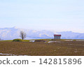 A barn with a red roof against a backdrop of snow-capped mountains, and fields in early winter. 142815896