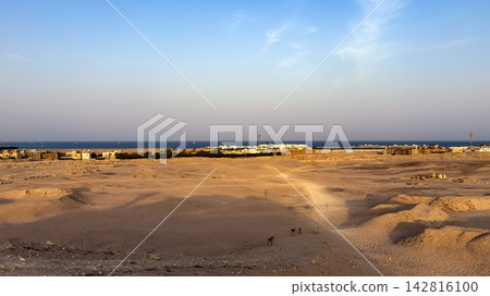 Arid desert landscape leading to a coastal town and sea horizon Arid desert landscape leading to a coastal town and sea horizon 142816100