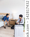 Two Asian men sitting in hotel room with silver suitcase, one wearing gray hoodie holding passport 142817432