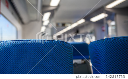Interior of a train carriage showing blue upholstered seats, with a bright and modern design illuminated by natural light from windows Interior of a train carriage showing blue upholstered seats, with a bright and modern design illuminated by natural light from windows 142817733