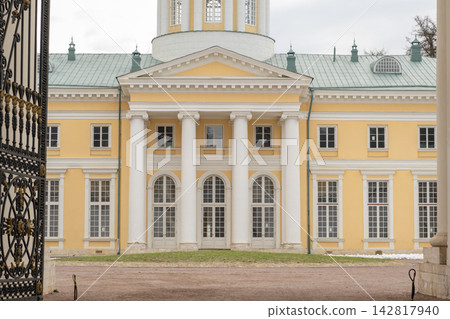 Historic yellow mansion features white columns and large windows, seen through ornate wrought iron gates in a landscaped garden area Historic yellow mansion features white columns and large windows, seen through ornate wrought iron gates in a landscaped garden area 142817940