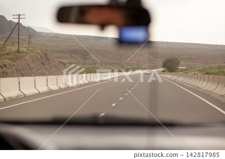 Perspective of a highway captured from inside a vehicle, showing a distant car and mountains along the roadside in a rural area Perspective of a highway captured from inside a vehicle, showing a distant car and mountains along the roadside in a rural area 142817985