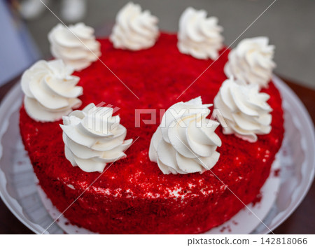 Red velvet cake features white cream swirls on top, displayed on a decorative plate, highlighting its vibrant red color and dessert appeal Red velvet cake features white cream swirls on top, displayed on a decorative plate, highlighting its vibrant red color and dessert appeal 142818066