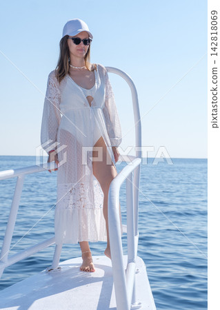 Young woman dressed in white beach attire stands on the deck of a boat, with the clear blue ocean visible in the background Young woman dressed in white beach attire stands on the deck of a boat, with the clear blue ocean visible in the background 142818069