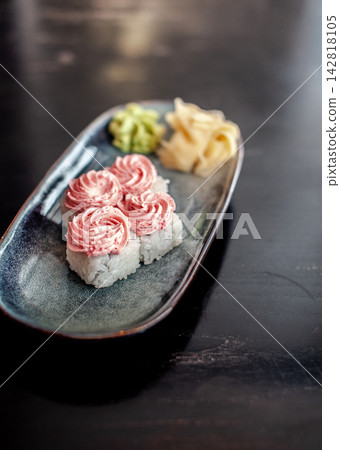 Sushi plate showcases decorative rolls with pink topping, served with wasabi and pickled ginger on a dark wooden table surface Sushi plate showcases decorative rolls with pink topping, served with wasabi and pickled ginger on a dark wooden table surface 142818105
