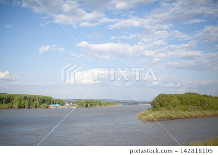Scenic view of a river winding through green banks, with a clear blue sky and white clouds creating a peaceful outdoor atmosphere Scenic view of a river winding through green banks, with a clear blue sky and white clouds creating a peaceful outdoor atmosphere 142818106