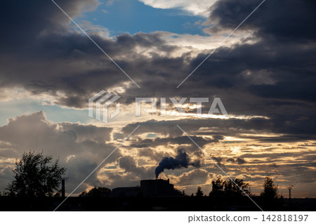 Silhouette of an industrial factory with smoke rising against a backdrop of dramatic clouds and a colorful sunset sky, highlighting environmental concerns Silhouette of an industrial factory with smoke rising against a backdrop of dramatic clouds and a colorful sunset sky, highlighting environmental concerns 142818197