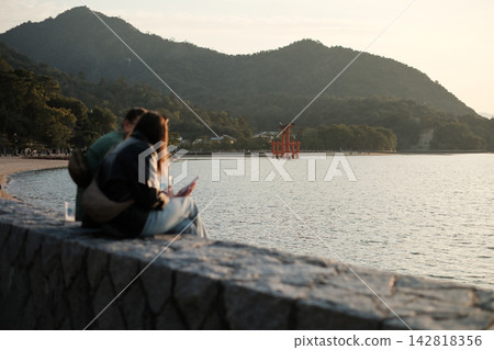 兩人正在宮島水邊欣賞鳥居。 兩人正在宮島水邊欣賞鳥居。 142818356