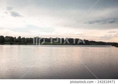 Calm lake landscape features lush green trees along the shore under a cloudy sky with soft light reflecting on the water surface Calm lake landscape features lush green trees along the shore under a cloudy sky with soft light reflecting on the water surface 142818471