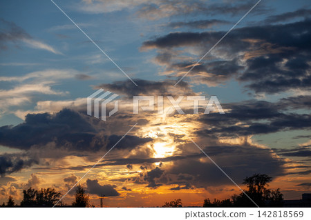 Dramatic sunset scene featuring vibrant clouds and golden light illuminating the sky, with silhouetted trees creating a striking foreground Dramatic sunset scene featuring vibrant clouds and golden light illuminating the sky, with silhouetted trees creating a striking foreground 142818569