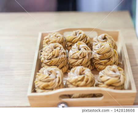 Handmade sweet pastries with intricate twisted designs are neatly arranged in a wooden tray, displaying a golden-brown color and appealing texture Handmade sweet pastries with intricate twisted designs are neatly arranged in a wooden tray, displaying a golden-brown color and appealing texture 142818608