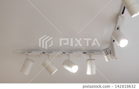 Modern ceiling track lighting features several adjustable spotlights mounted on a white ceiling, providing illumination in a contemporary interior setting Modern ceiling track lighting features several adjustable spotlights mounted on a white ceiling, providing illumination in a contemporary interior setting 142818632