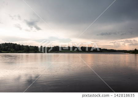 Tranquil view of a calm lake with reflections of cloudy skies and lush trees along the shoreline in a serene natural environment Tranquil view of a calm lake with reflections of cloudy skies and lush trees along the shoreline in a serene natural environment 142818635