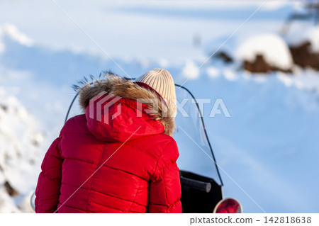 Child wearing a red winter jacket with fur hood gazes at a snowy landscape, with snow-covered ground and distant trees in the background Child wearing a red winter jacket with fur hood gazes at a snowy landscape, with snow-covered ground and distant trees in the background 142818638