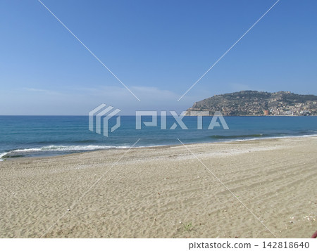 Serene beach scene featuring golden sand, clear blue water, and distant hills under a bright sky in a coastal area 142818640