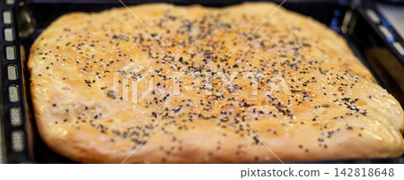 Freshly baked flatbread with sesame seeds on top, resting on a black baking tray, highlighting its golden-brown crust and soft surface Freshly baked flatbread with sesame seeds on top, resting on a black baking tray, highlighting its golden-brown crust and soft surface 142818648