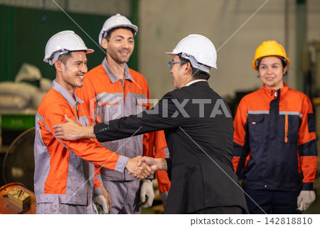 Chief engineer congratulating young engineer with handshake. Outstanding performance recognition during factory team meeting. Chief engineer congratulating young engineer with handshake. Outstanding performance recognition during factory team meeting. 142818810