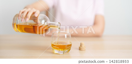 woman pour whiskey into a glass on table, suffering from alcohol addiction, alcoholism concept. depicting emotional distress, depression, substance abuse problem, unhealthy lifestyle and mental health woman pour whiskey into a glass on table, suffering from alcohol addiction, alcoholism concept. depicting emotional distress, depression, substance abuse problem, unhealthy lifestyle and mental health 142818933