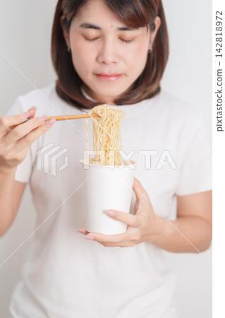 Happy young Asian woman enjoying a delicious cup of hot instant noodles while relaxing at home, Cheerful female eating instant ramen with a smile at apartment. Simple lifestyle and quick meal concept Happy young Asian woman enjoying a delicious cup of hot instant noodles while relaxing at home, Cheerful female eating instant ramen with a smile at apartment. Simple lifestyle and quick meal concept 142818972