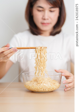 Happy young Asian woman enjoying a delicious bowl of hot instant noodles while relaxing at home, Cheerful female eating instant ramen with a smile at apartment. Simple lifestyle and quick meal concept Happy young Asian woman enjoying a delicious bowl of hot instant noodles while relaxing at home, Cheerful female eating instant ramen with a smile at apartment. Simple lifestyle and quick meal concept 142818975