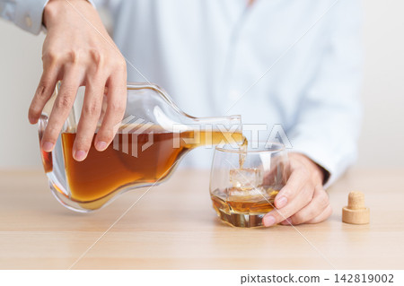 man pour cognac into a glass on table, suffering from alcohol addiction, alcoholism concept. depicting emotional distress, depression, substance abuse problem, unhealthy lifestyle and mental health 142819002