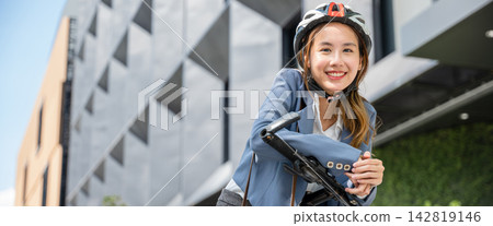 Morning outdoor motion An Asian businesswoman suited up and helmeted stands with her bicycle symbolizing the concept of a cheerful business commuter. 142819146