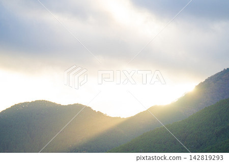 Sunlight streams through the clouds onto the forested mountain range. Sunlight streams through the clouds onto the forested mountain range. 142819293