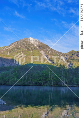 Early summer in Kamikochi: The breathtaking view of Mt. Yake reflected in Taisho Pond and the fresh greenery of the Northern Alps in the morning. Early summer in Kamikochi: The breathtaking view of Mt. Yake reflected in Taisho Pond and the fresh greenery of the Northern Alps in the morning. 142819874