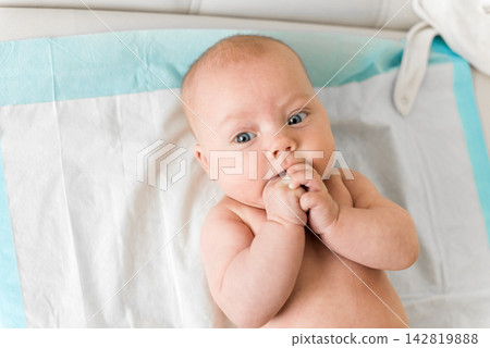 Baby 5-6 months old lies on back and sucks fingers during everyday care at home, natural self soothing behavior Baby 5-6 months old lies on back and sucks fingers during everyday care at home, natural self soothing behavior 142819888