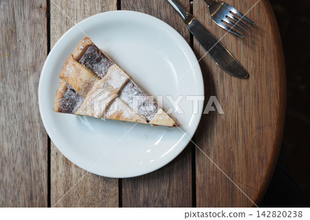 Slice of apple pie on a white plate placed on a wooden table 142820238