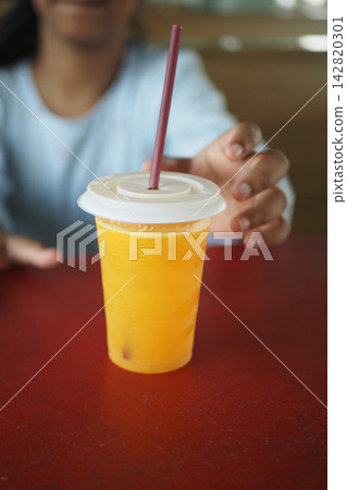A child reaches for a cup of orange drink in a cafe during the day A child reaches for a cup of orange drink in a cafe during the day 142820301