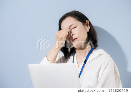 一位女性上班族眼睛疲勞，神情困倦；一位日本女商人一邊用筆記型電腦工作，一邊用力按壓眼角。 142820439