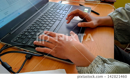 Pair of hands typing on modern laptop keyboard at wooden desk Pair of hands typing on modern laptop keyboard at wooden desk 142821460