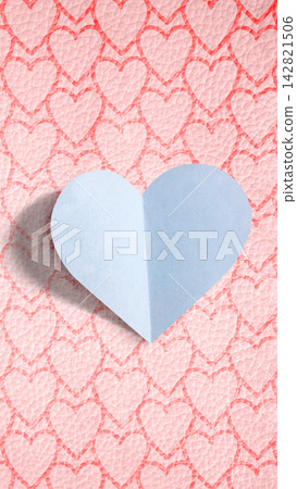 A blue folded paper heart on a pink background patterned with smaller hearts. Love background A blue folded paper heart on a pink background patterned with smaller hearts. Love background 142821506