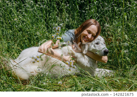 Joyful Woman Hugging a Maremma Sheepdog in a Wildflower Meadow Joyful Woman Hugging a Maremma Sheepdog in a Wildflower Meadow 142821675