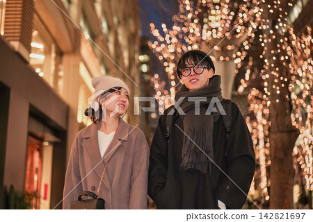 一對年輕情侶走在燈火通明的街道上。 142821697