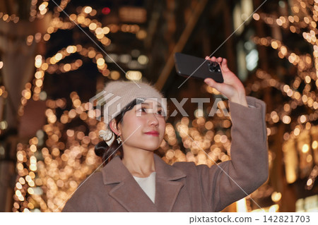 一位年輕女子正在用智慧型手機拍攝聖誕燈飾。 142821703