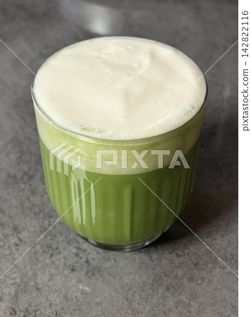 Matcha latte in a clear cup with vibrant green color, topped with creamy froth, highlighting smooth texture, swirling patterns, and refreshing appearance in close-up detail 142822116