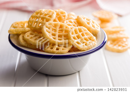 Crispy Waffle Potato Chips in a White Enamel Bowl on a Light Wooden Table 142823931
