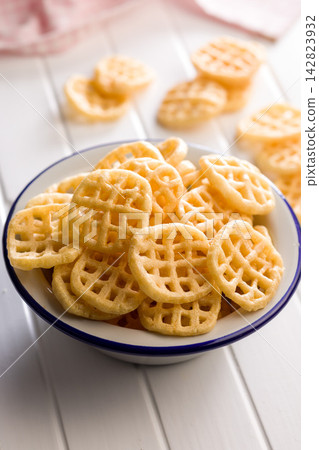Crispy Waffle Potato Chips in a White Enamel Bowl on a Light Wooden Table Crispy Waffle Potato Chips in a White Enamel Bowl on a Light Wooden Table 142823932
